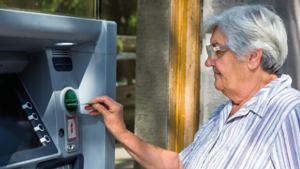 Kampania zus bezpiecznie, zdrowo, bezgotówkowo. Starsza kobieta korzystająca z bankomatu.