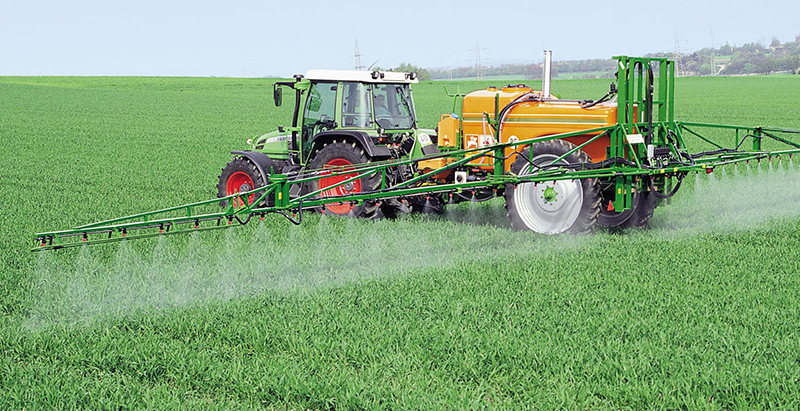 Ciągnik z opryskiwaczem na polu pryska zielone zboże